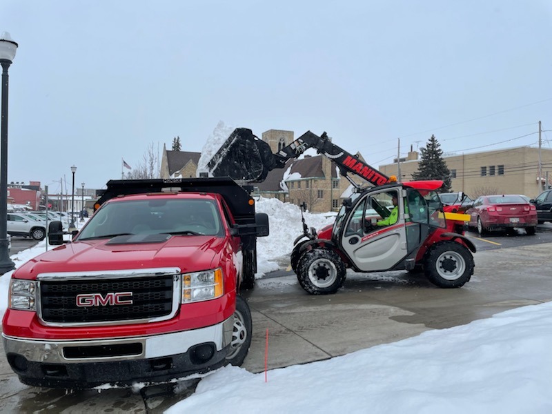 Loader loads snow into truck in snowy town.