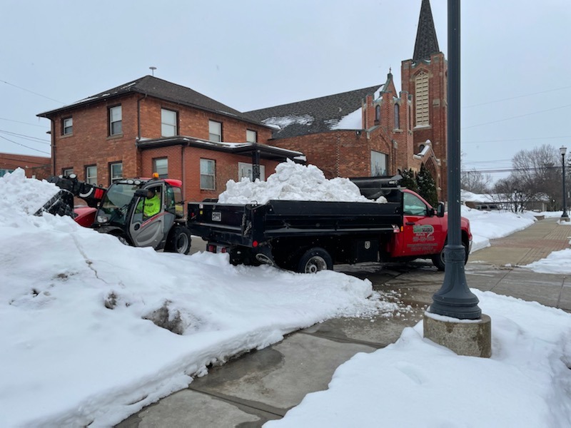 Snow removal vehicles in front of a brick building.
