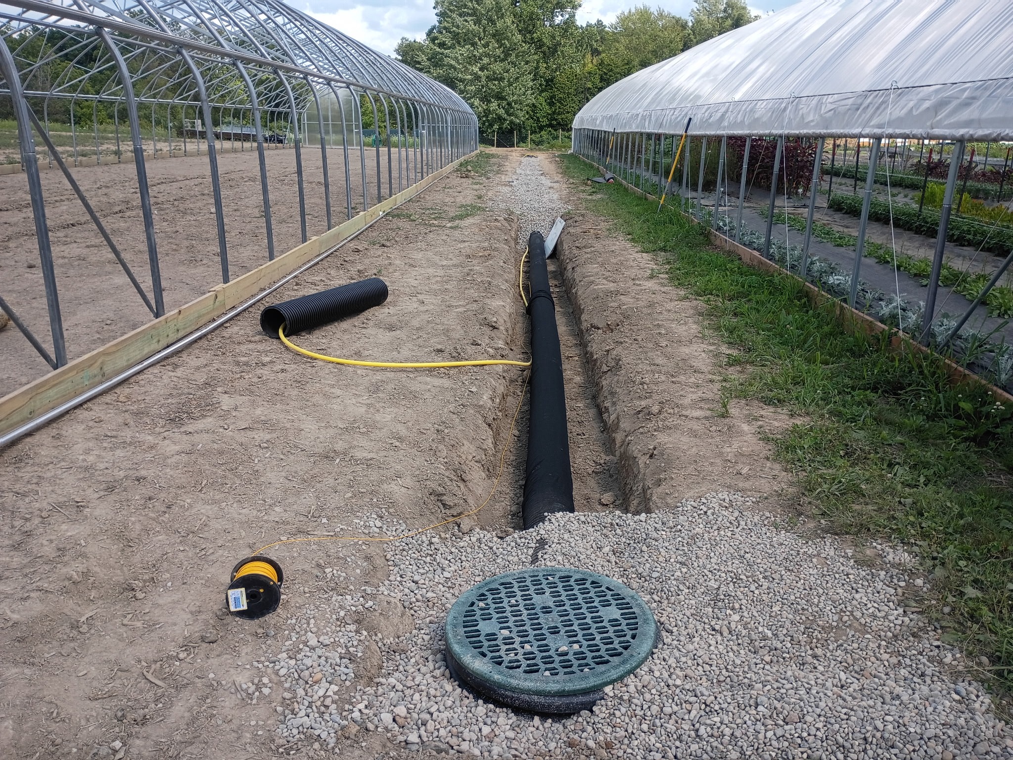 Greenhouse drainage system installation with trench and piping.