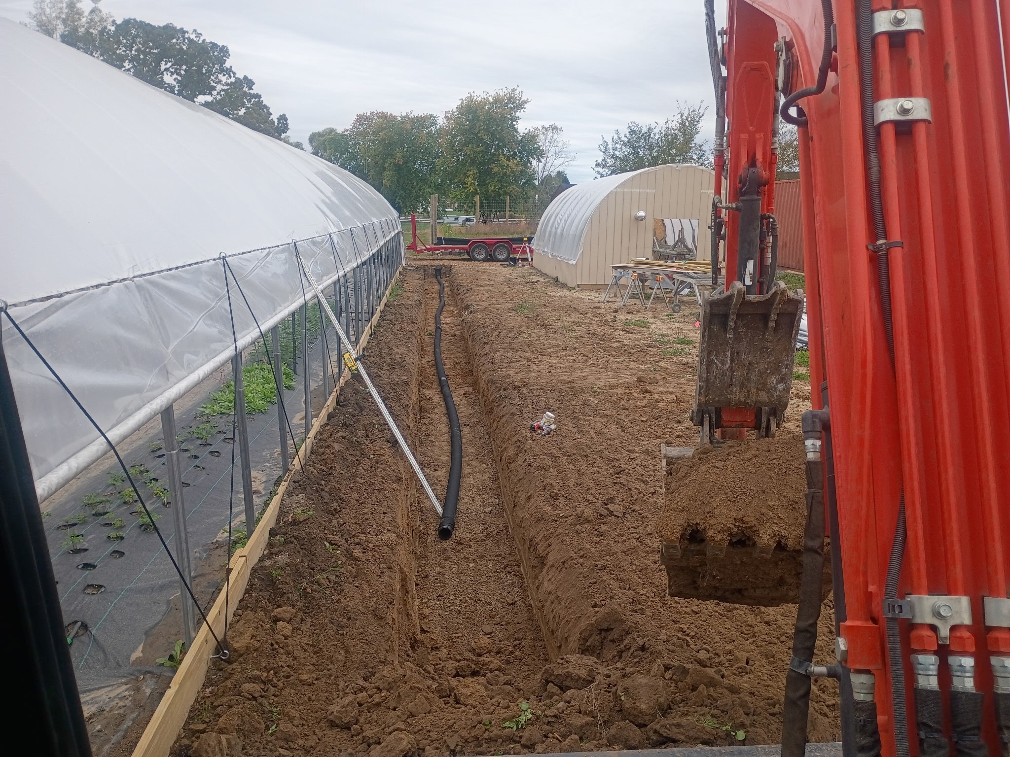 Excavator digging trench near greenhouses