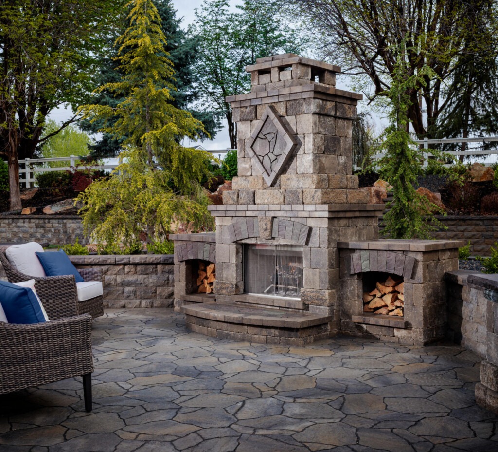 Stone outdoor fireplace on patio with chairs.