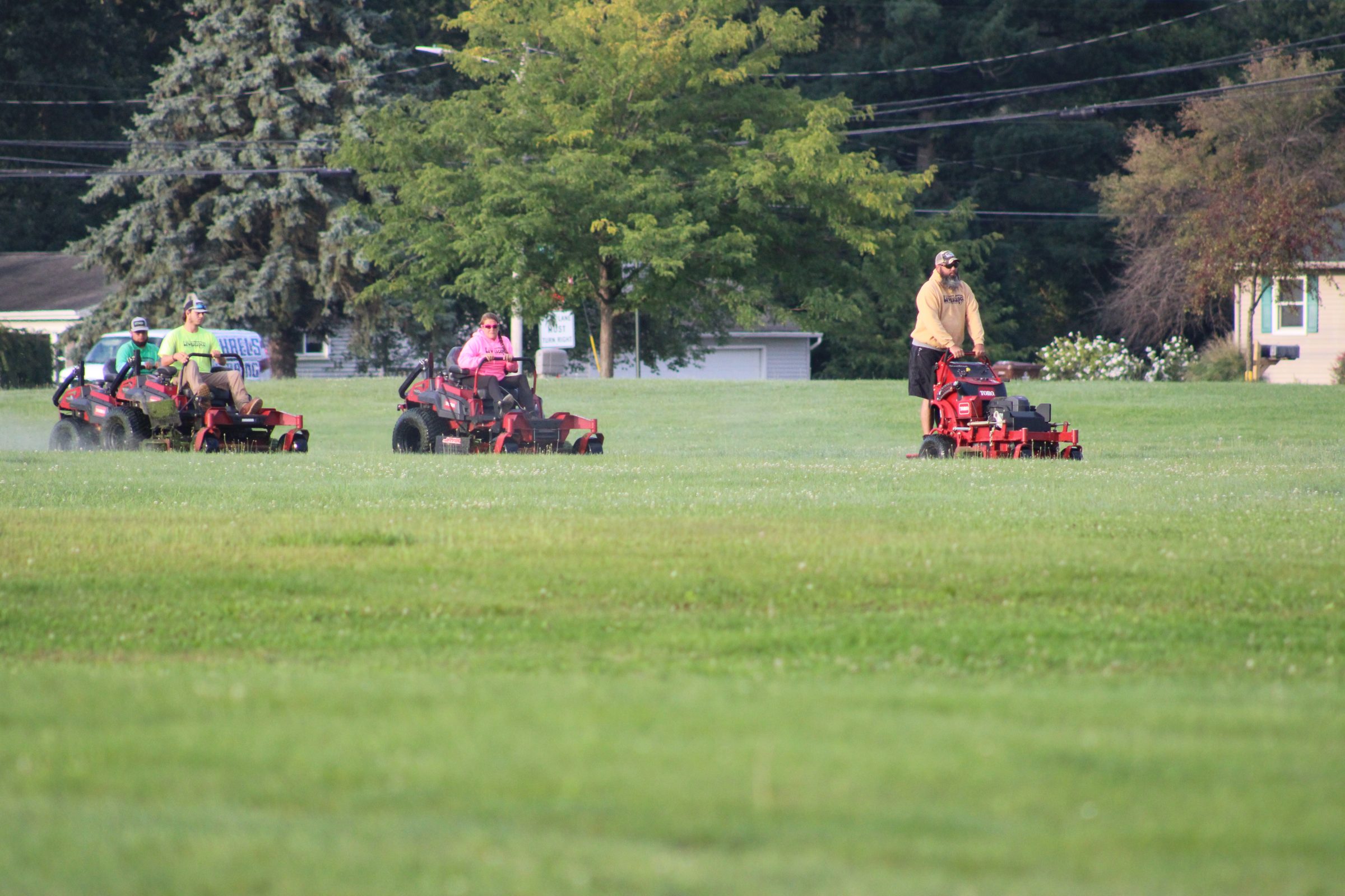 People mowing large field with lawn mowers.