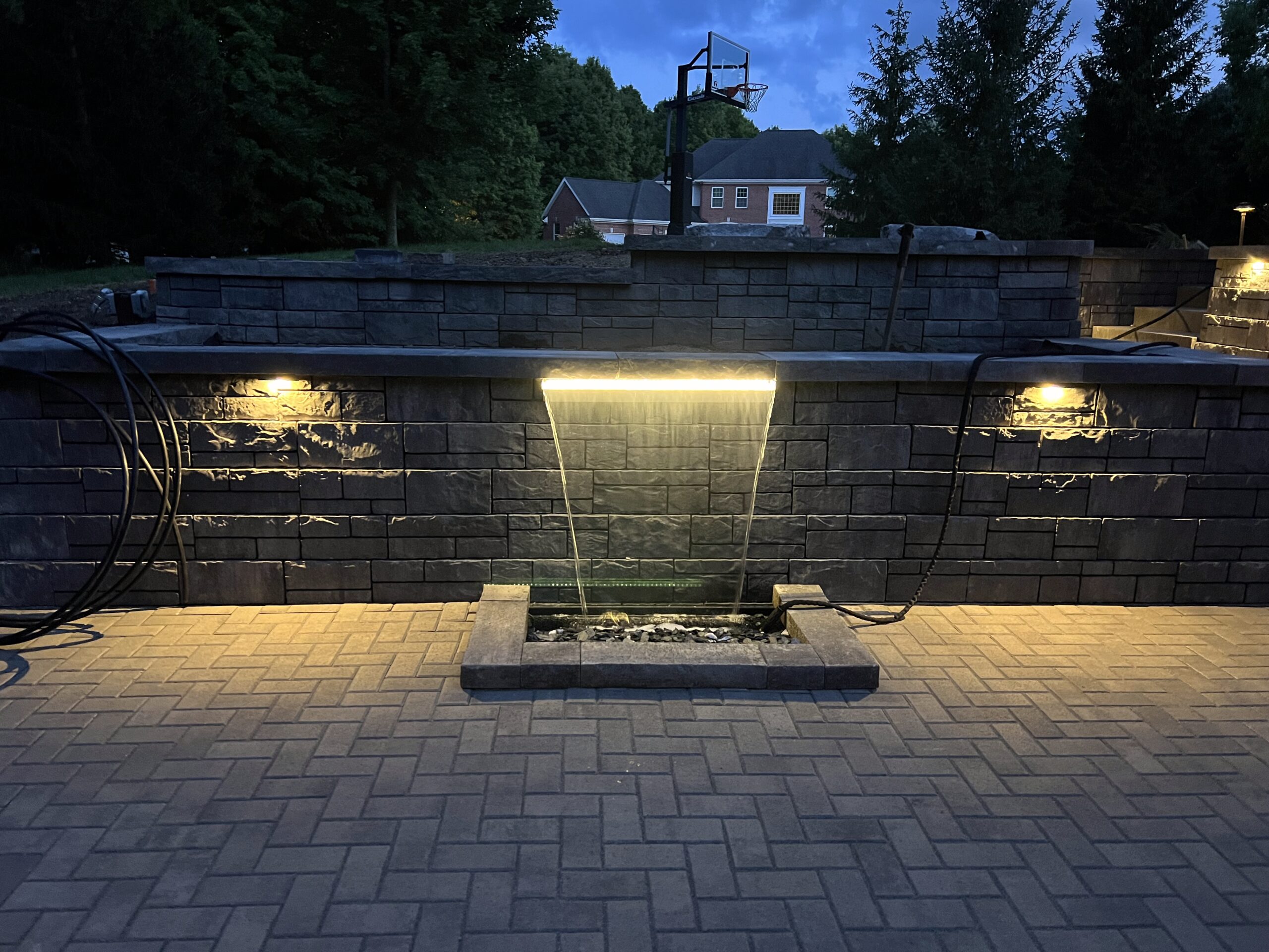 Evening brick patio with illuminated stone water feature.