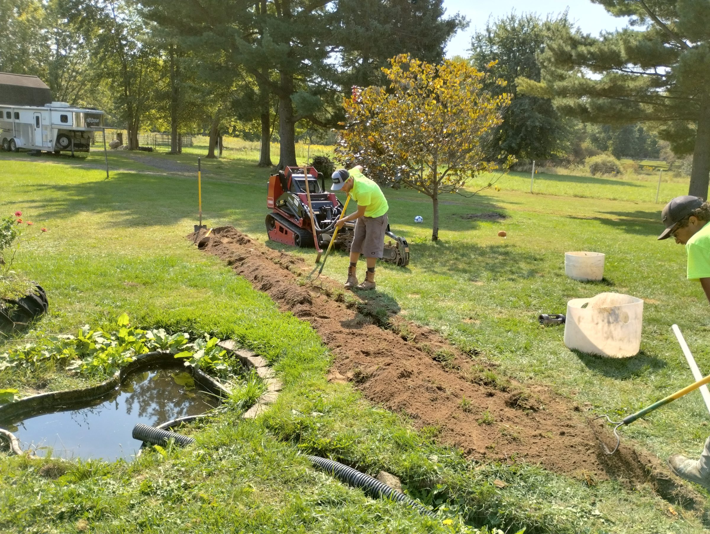 Workers digging trench in grassy area.