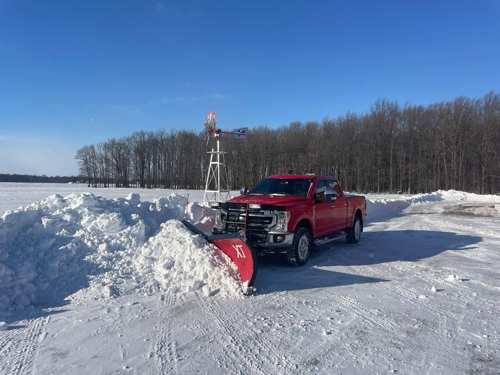 Red truck with snow plow in snowy landscape.