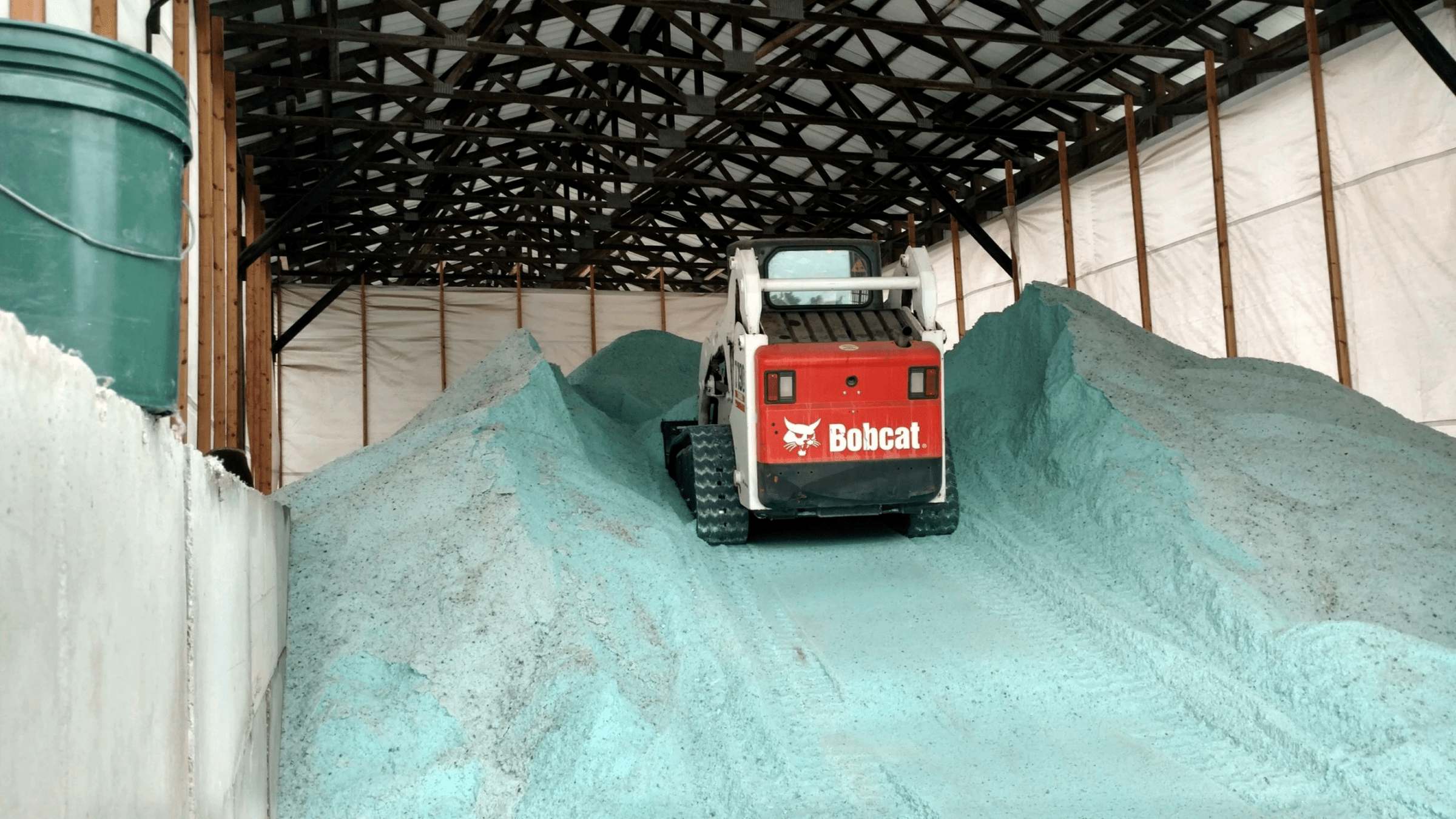 Bobcat loader with green salt piles in shed.