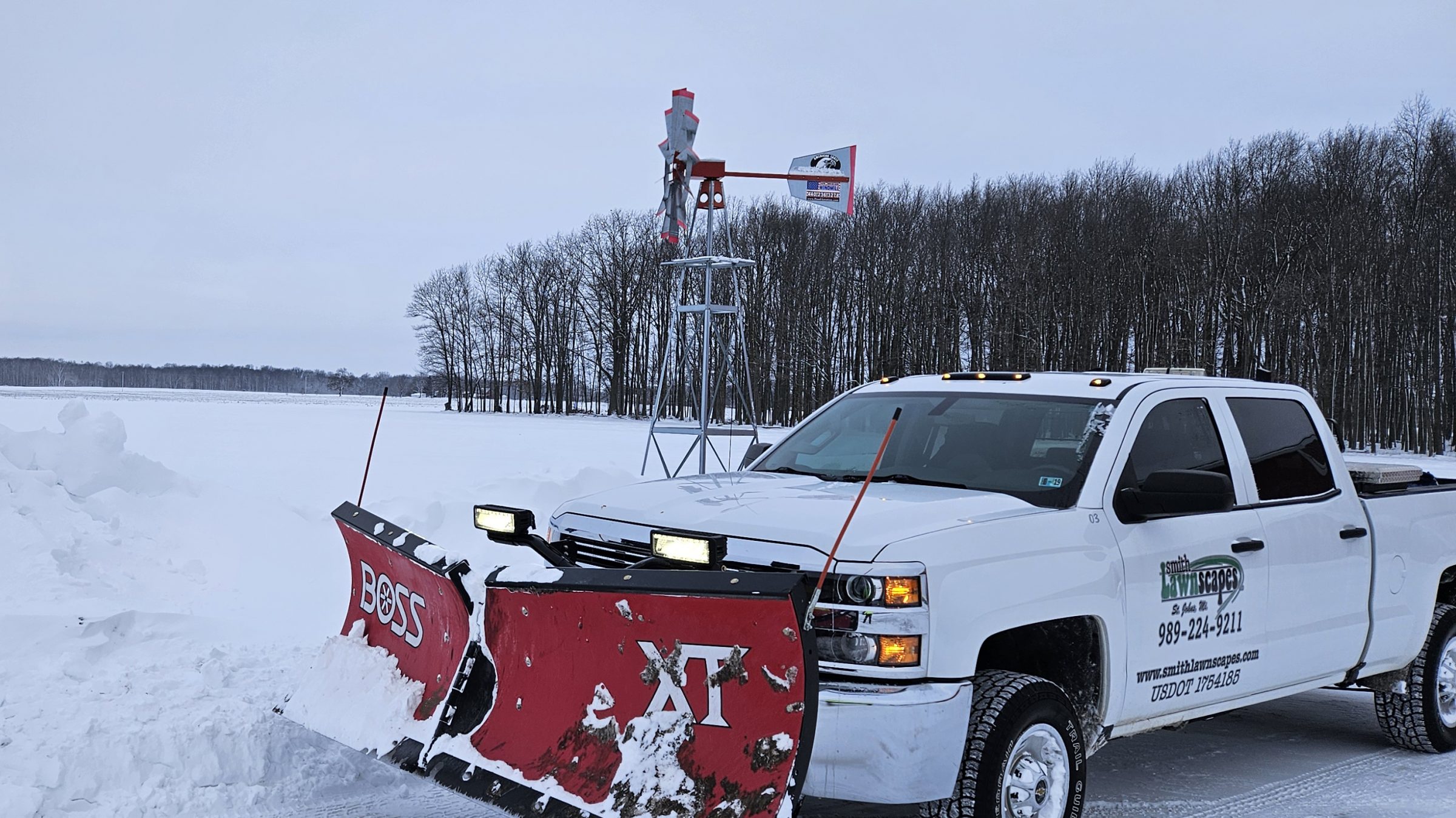 Snow plow truck clearing snowy road with windmill.
