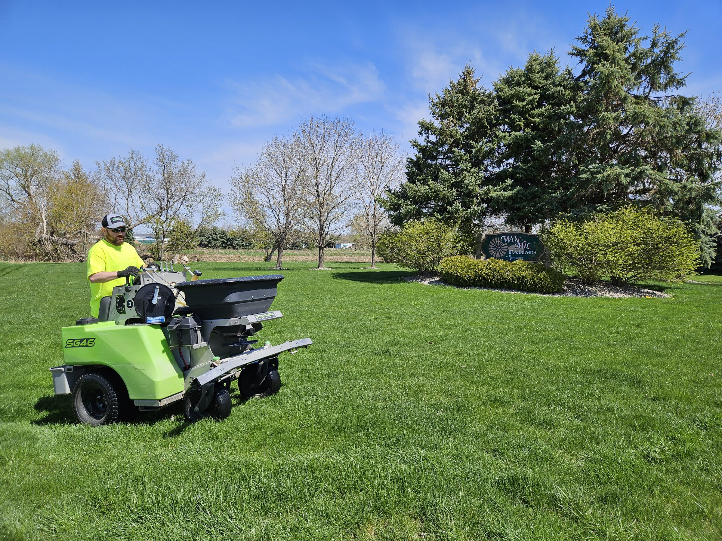 Worker fertilizing lawn with green spreader machine