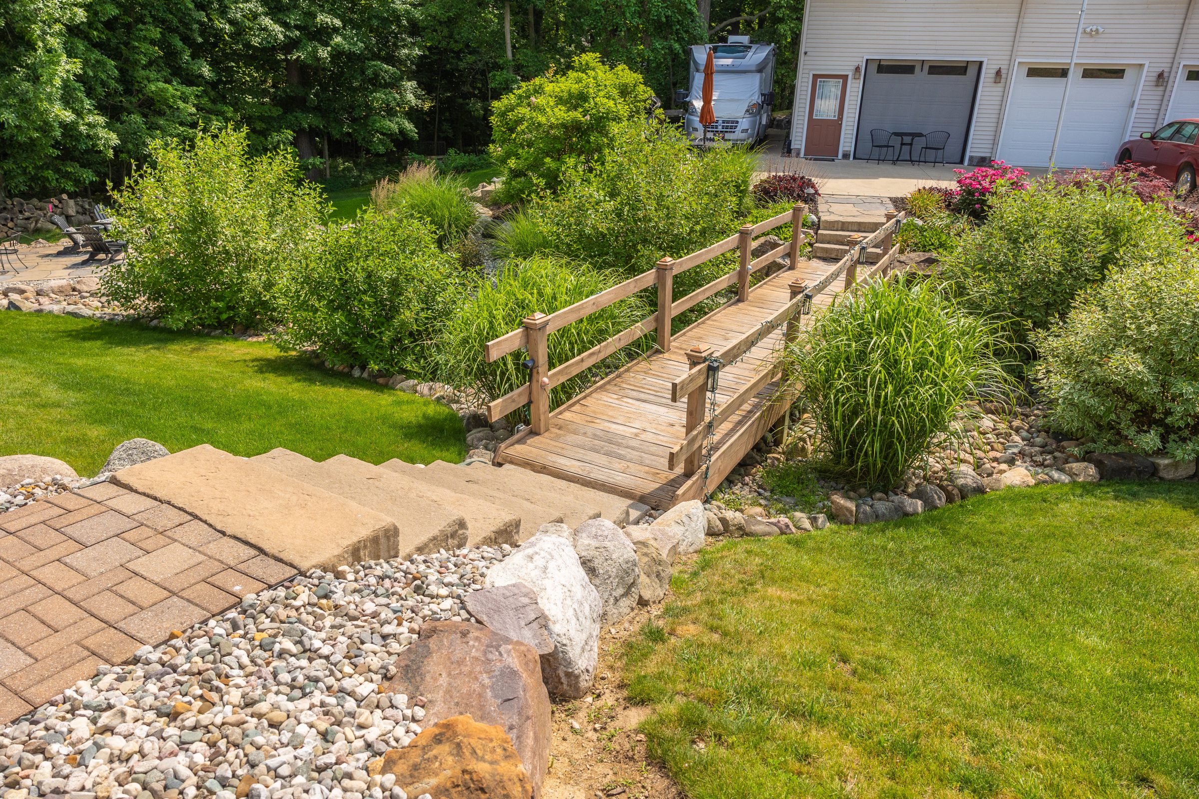 Wooden bridge in landscaped garden near house and RV.