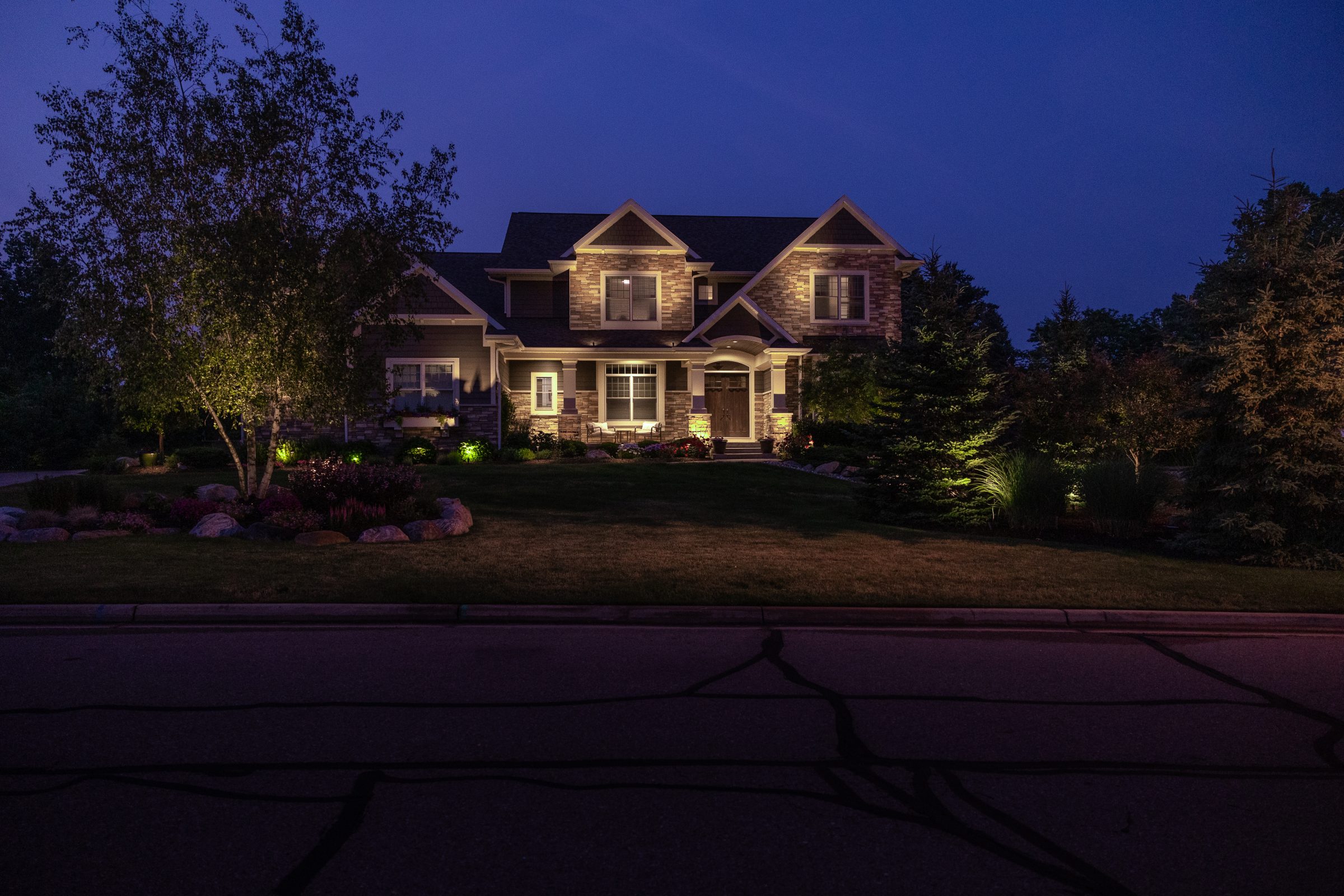 Illuminated house at dusk with trees and lawn.