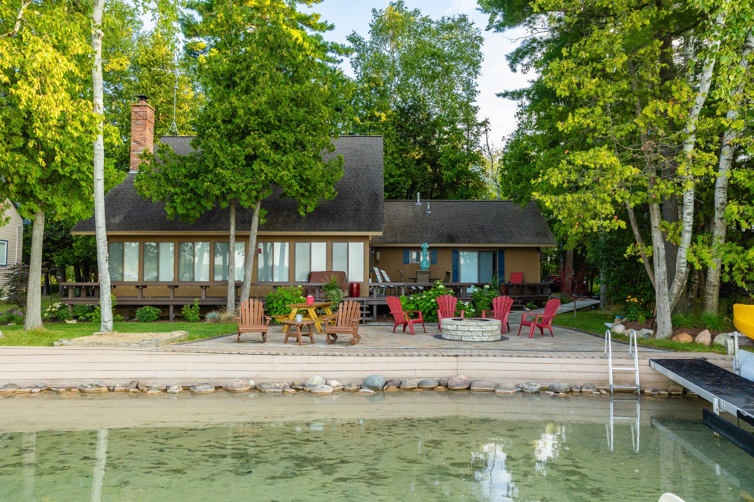 Lakeside cabin with trees and outdoor seating area.
