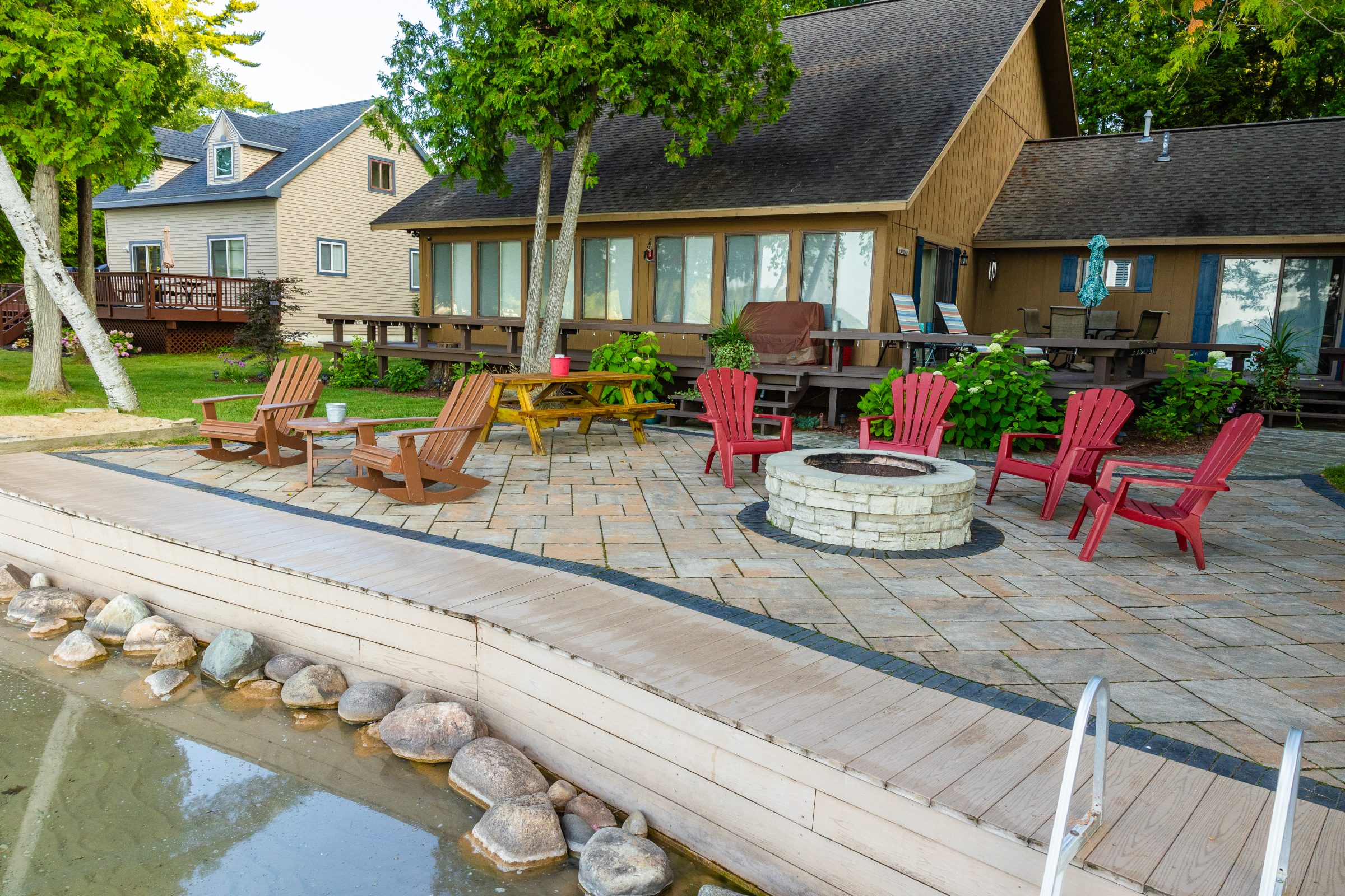 Outdoor patio with fire pit and chairs by lake.