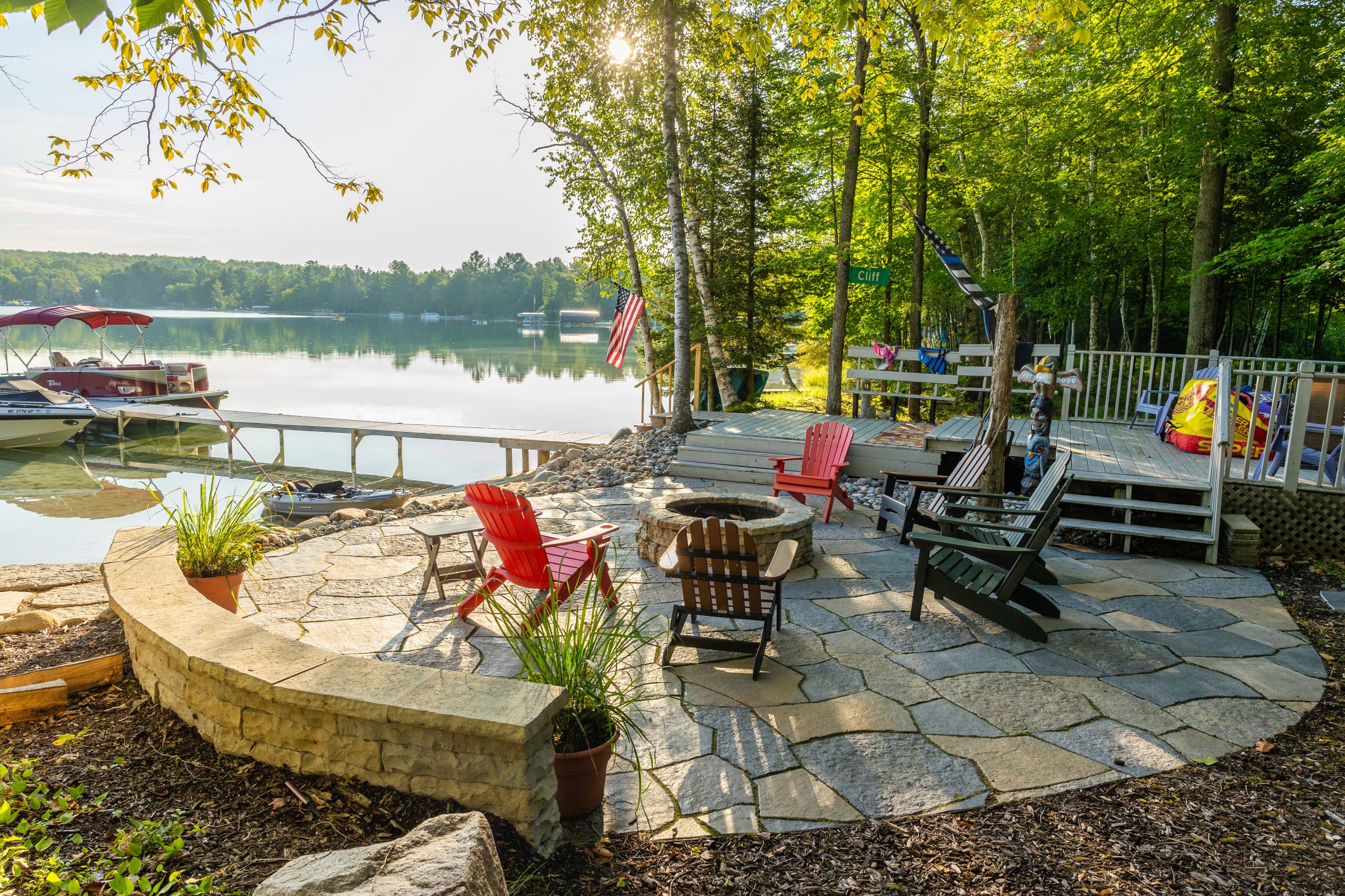Lakeside patio with chairs and boats, sunny day.