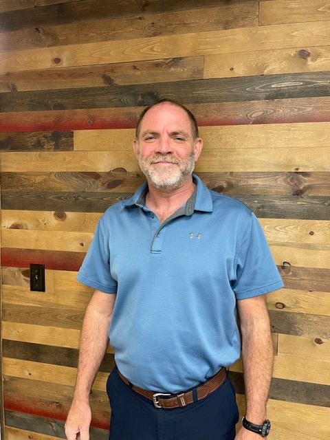 Man in blue shirt standing against wooden wall.