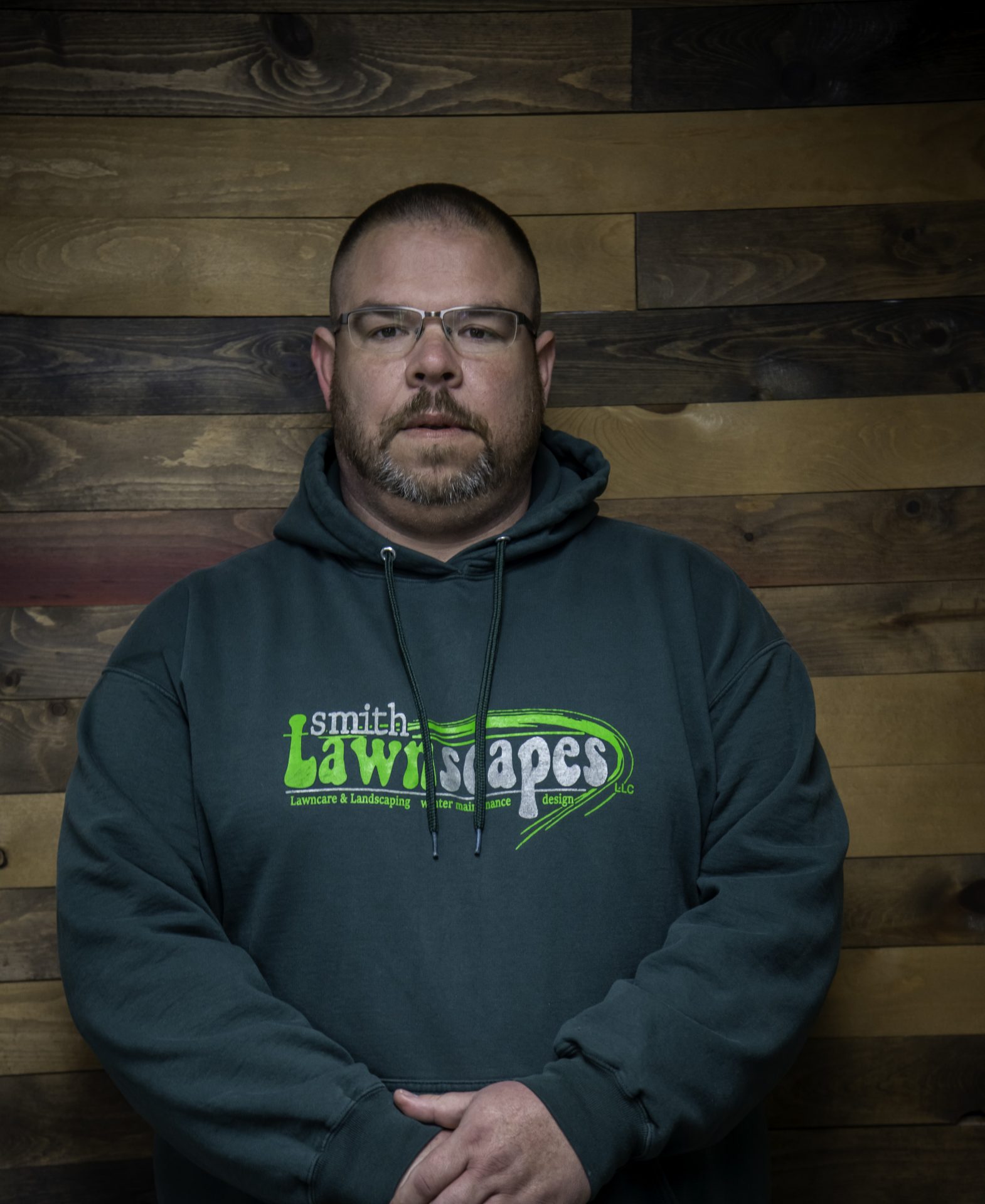 Man in sweatshirt against wooden wall.