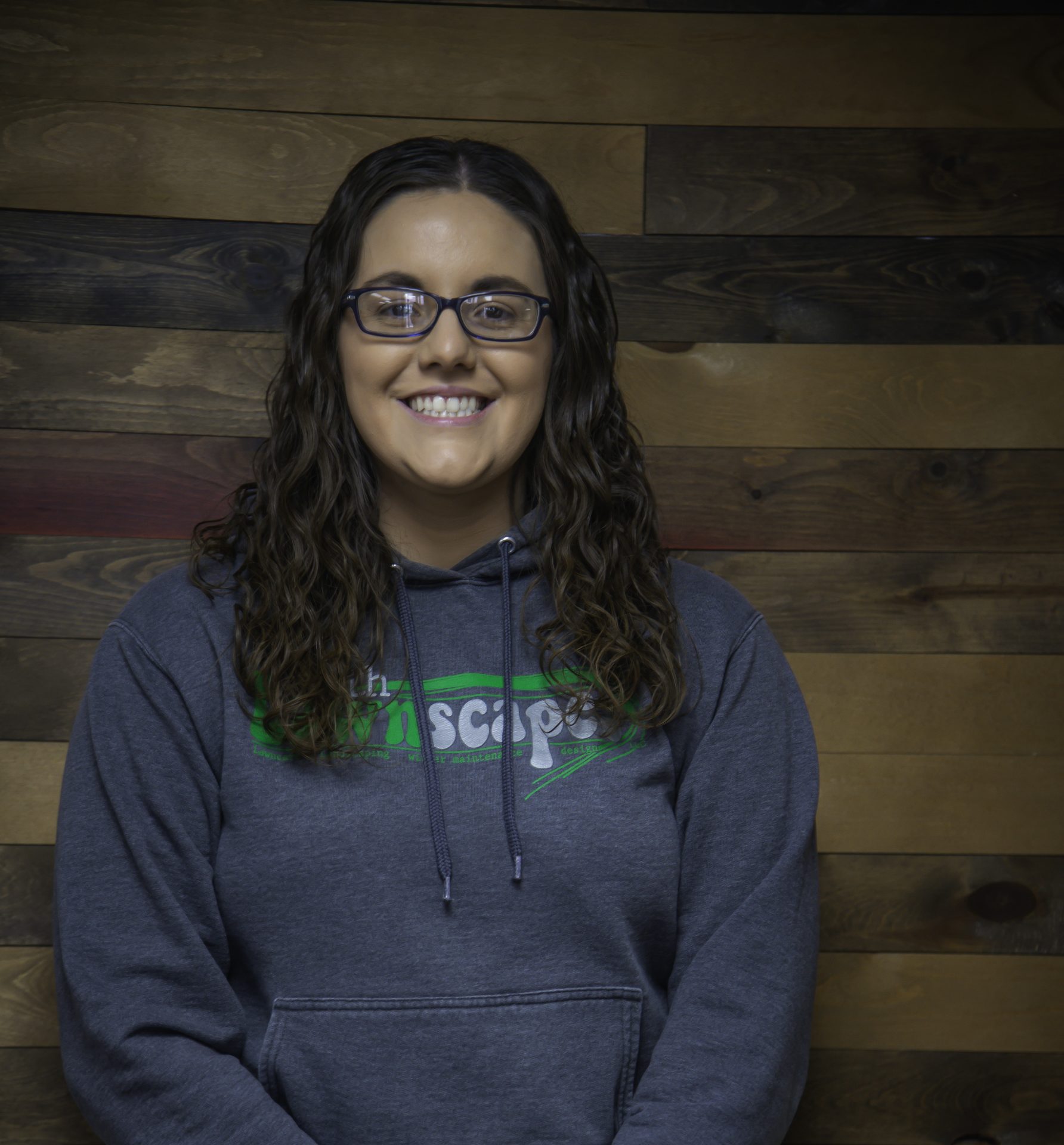 Person smiling wearing a hoodie against wood background.