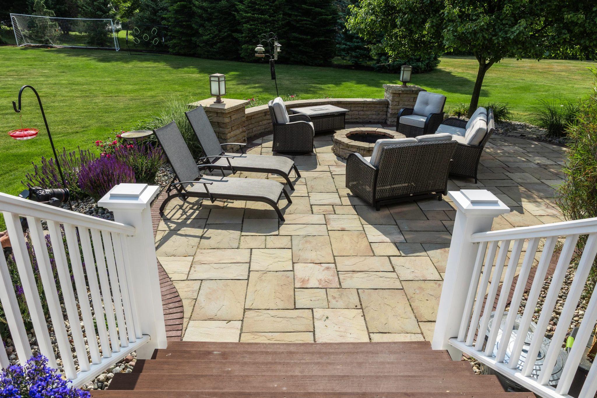 Curved stone patio with fire pit, cushioned outdoor seating, and surrounding lawn designed for relaxation and gatherings.
